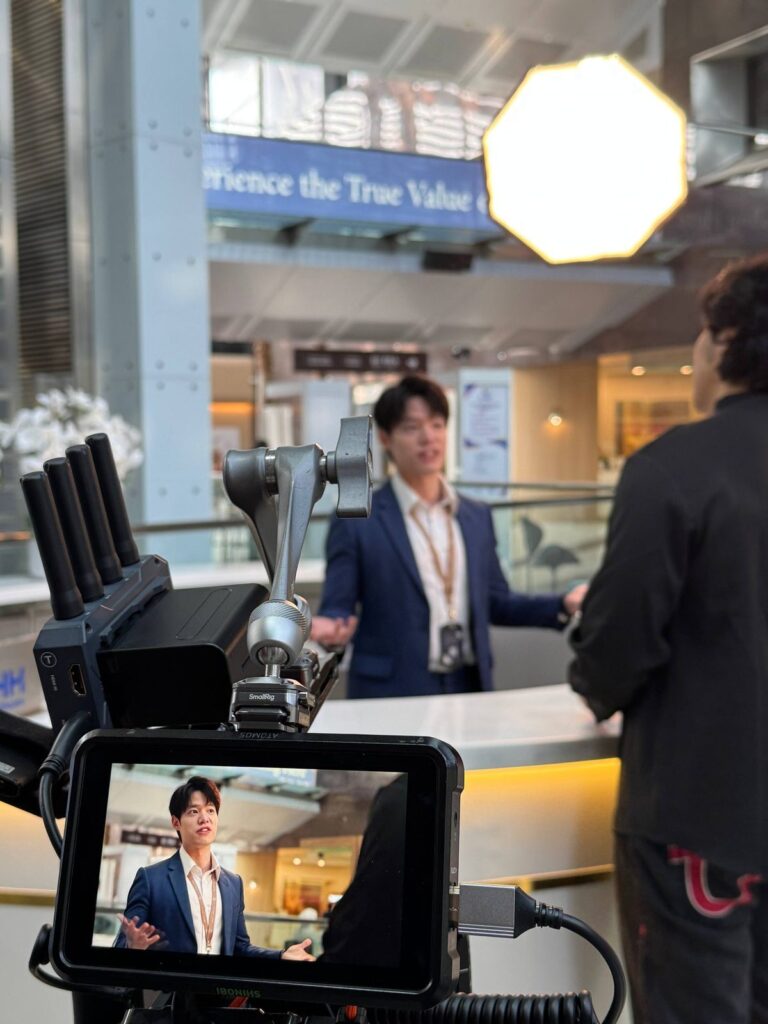 A camera monitor shows the host framed in the lobby