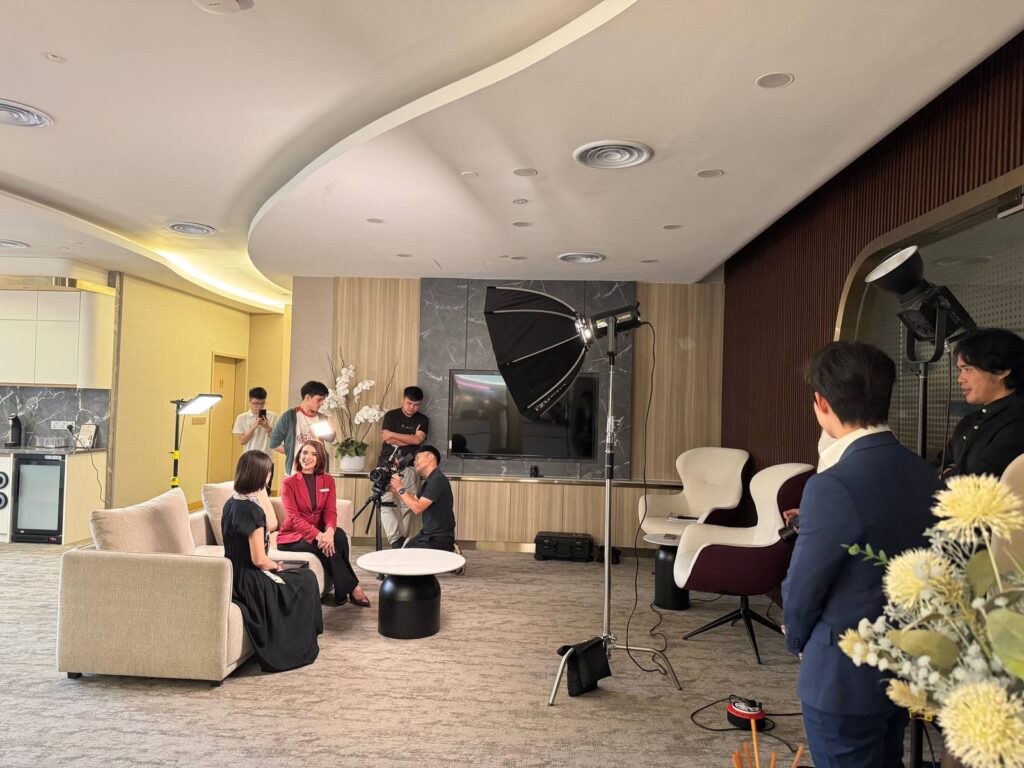 The Premium Lounge host chats with a patient on a sofa while the crew films